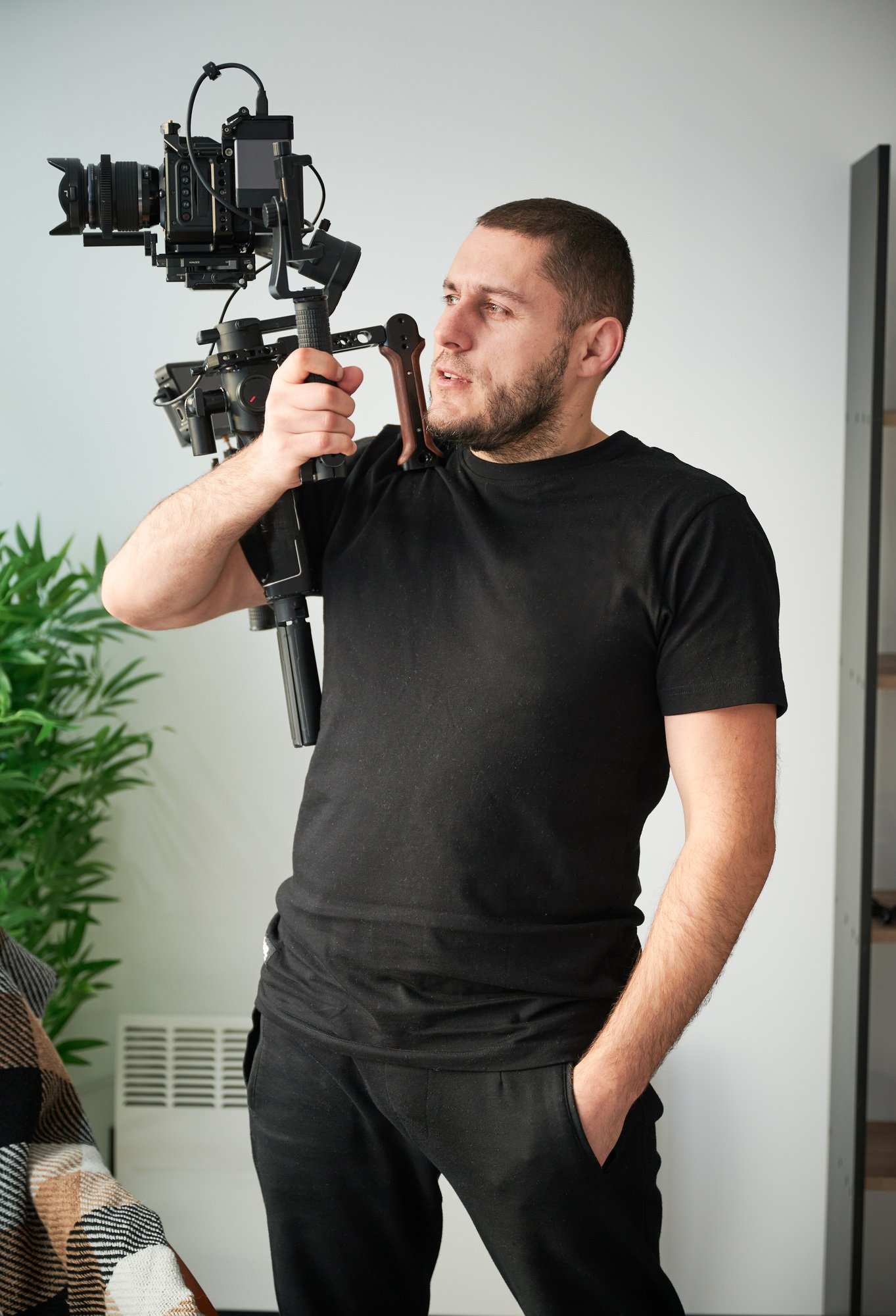 Videographer man with camera mounted on gimbal stabilizer equipment indoors.
